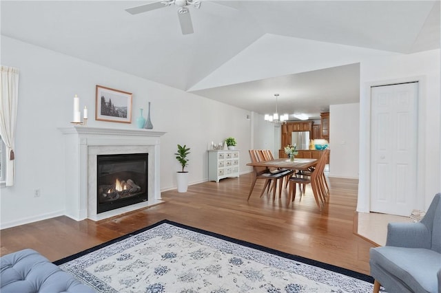 living room with hardwood / wood-style flooring, ceiling fan with notable chandelier, lofted ceiling, and a premium fireplace