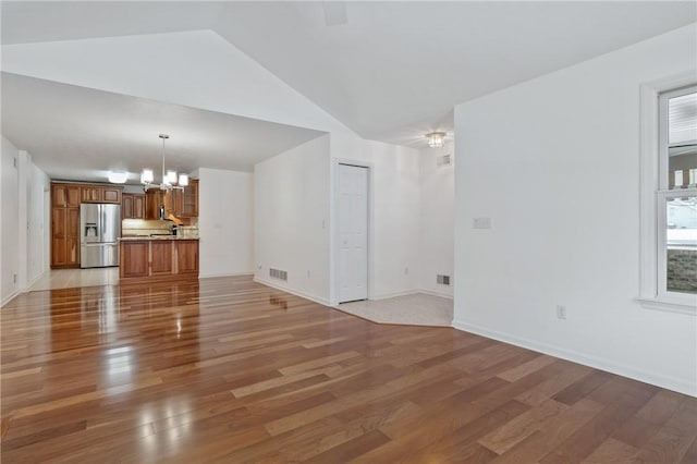 unfurnished living room featuring hardwood / wood-style flooring, lofted ceiling, and a notable chandelier