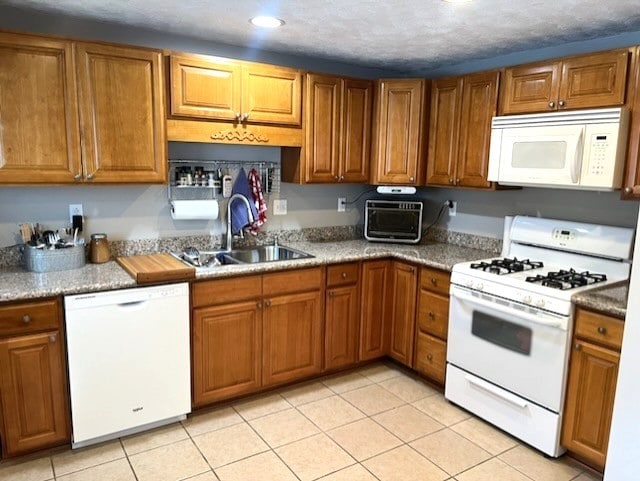 kitchen with sink, white appliances, light tile patterned floors, and a textured ceiling