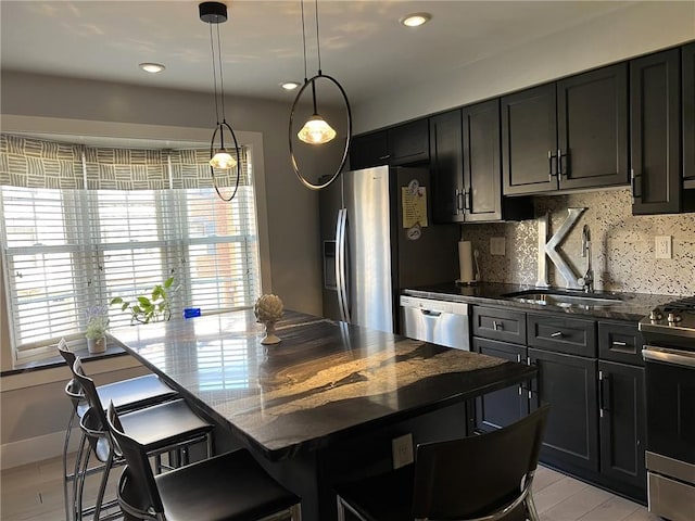 kitchen featuring a kitchen bar, appliances with stainless steel finishes, hanging light fixtures, sink, and a kitchen island