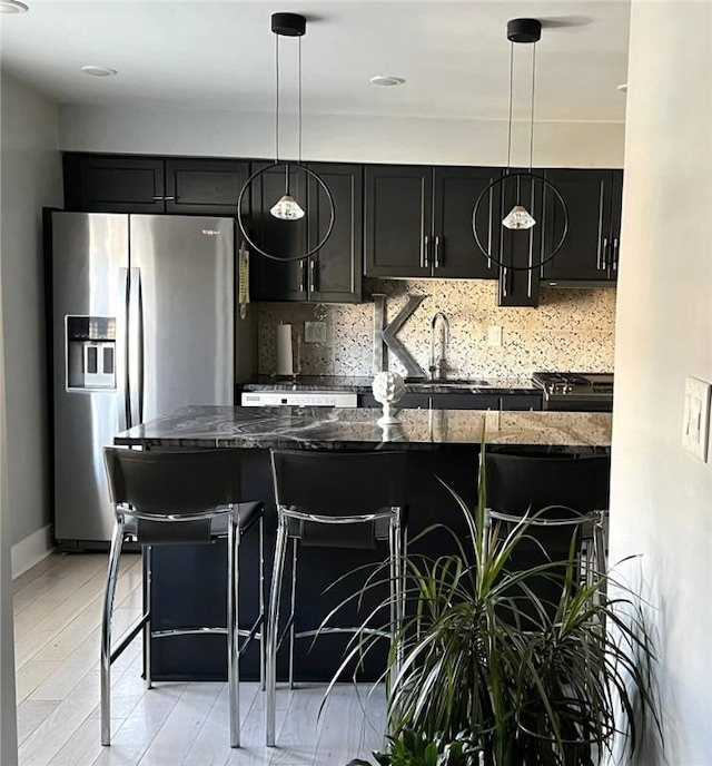 kitchen with pendant lighting, a breakfast bar area, stainless steel fridge, and dark stone countertops