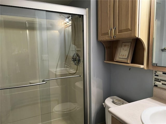 bathroom featuring toilet, decorative backsplash, a shower with shower door, and vanity