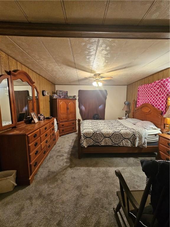 bedroom with ceiling fan, wood walls, and carpet flooring