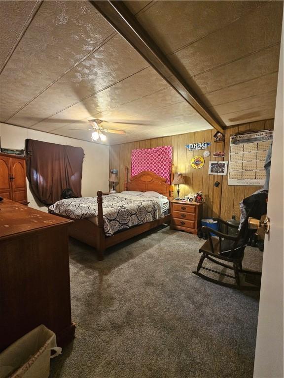 carpeted bedroom featuring ceiling fan, wood walls, and beam ceiling