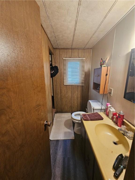 bathroom featuring a textured ceiling, toilet, wooden walls, and vanity