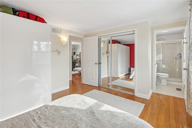 bedroom featuring ensuite bathroom, crown molding, a closet, and light wood-type flooring