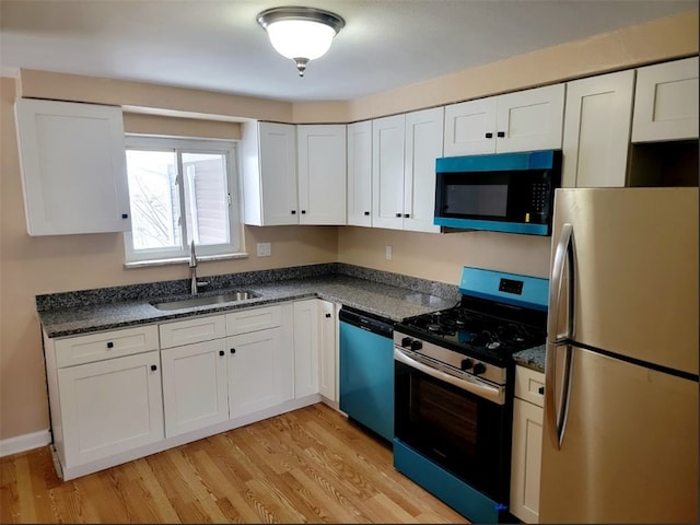 kitchen with white cabinets, stainless steel appliances, dark stone counters, sink, and light hardwood / wood-style flooring