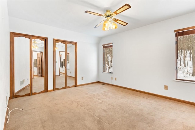 unfurnished bedroom featuring lofted ceiling, multiple closets, light colored carpet, and ceiling fan