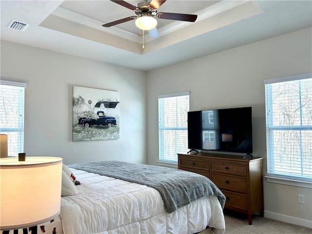 carpeted bedroom featuring multiple windows, a tray ceiling, and ceiling fan