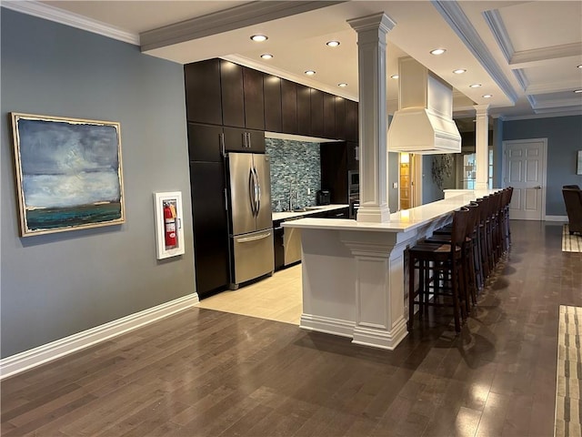 kitchen featuring stainless steel fridge, premium range hood, a kitchen breakfast bar, ornamental molding, and ornate columns