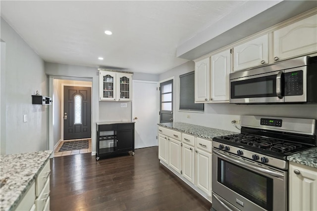 kitchen with dark wood-type flooring, white cabinetry, appliances with stainless steel finishes, and light stone countertops