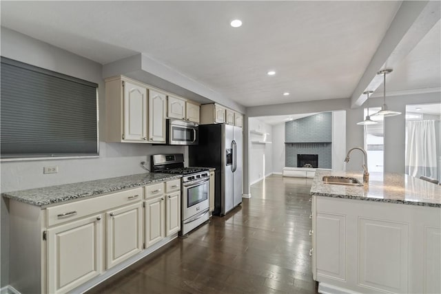 kitchen featuring sink, appliances with stainless steel finishes, light stone counters, a brick fireplace, and decorative light fixtures