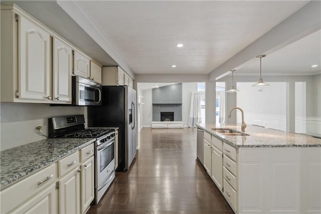 kitchen with appliances with stainless steel finishes, pendant lighting, sink, light stone counters, and a brick fireplace