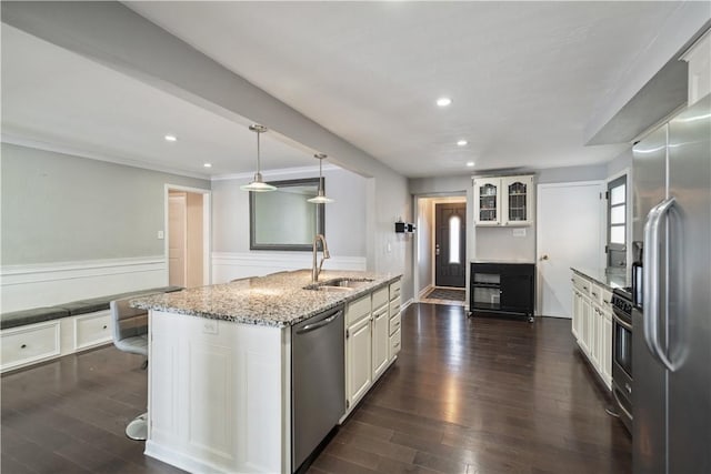 kitchen with sink, hanging light fixtures, an island with sink, stainless steel appliances, and light stone countertops