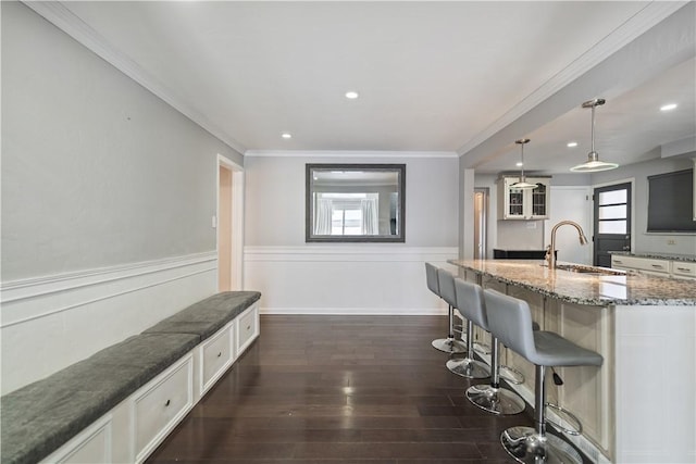 kitchen with a breakfast bar, white cabinetry, sink, hanging light fixtures, and a kitchen island with sink