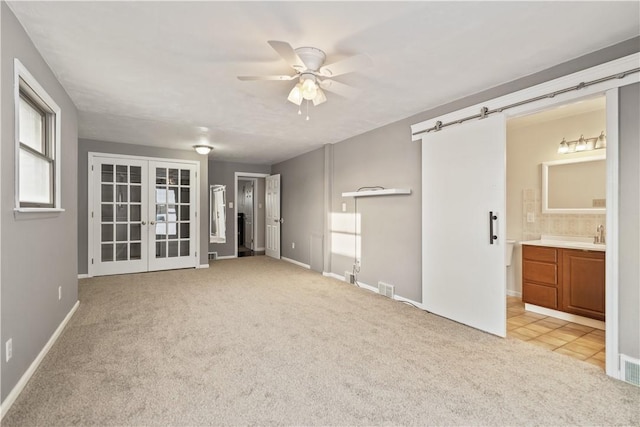 spare room with light colored carpet, a barn door, ceiling fan, and french doors