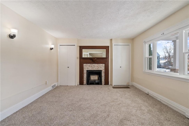 unfurnished living room featuring carpet floors, a textured ceiling, and a tiled fireplace