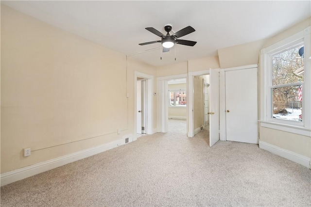 unfurnished bedroom featuring multiple windows, light colored carpet, and ceiling fan