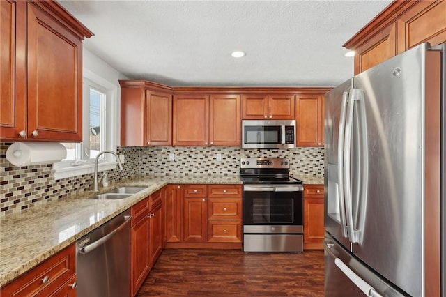 kitchen with appliances with stainless steel finishes, sink, light stone counters, dark hardwood / wood-style floors, and decorative backsplash