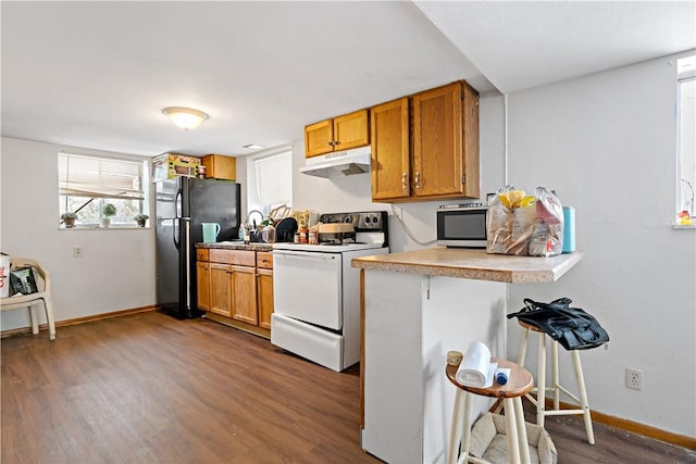 kitchen with a kitchen breakfast bar, kitchen peninsula, black refrigerator, dark wood-type flooring, and electric stove