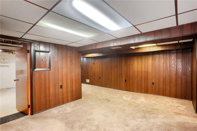 basement featuring a paneled ceiling, light carpet, and wood walls