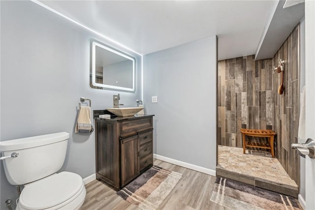 bathroom featuring a shower, hardwood / wood-style floors, toilet, vanity, and wood walls