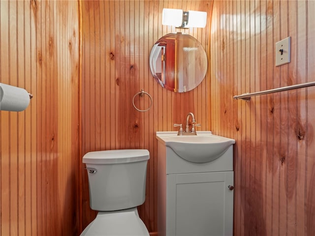 bathroom with wood walls, toilet, and vanity