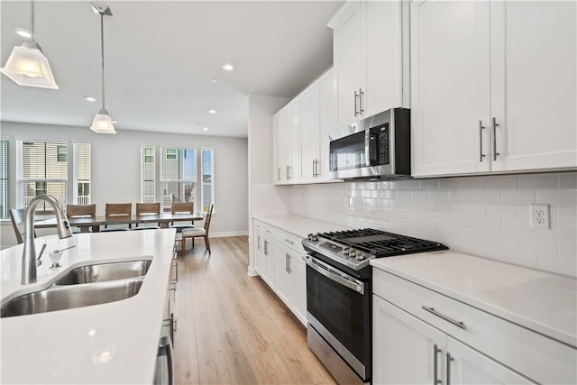 kitchen with appliances with stainless steel finishes, tasteful backsplash, sink, decorative light fixtures, and white cabinets