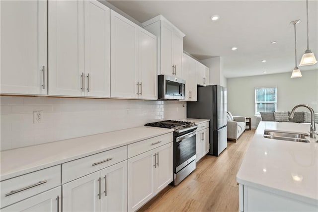 kitchen featuring white cabinets, decorative light fixtures, stainless steel appliances, decorative backsplash, and sink