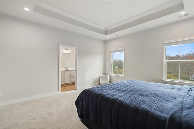 bedroom with light carpet, ensuite bath, multiple windows, and a tray ceiling