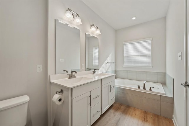 bathroom featuring vanity, toilet, tiled tub, and wood-type flooring