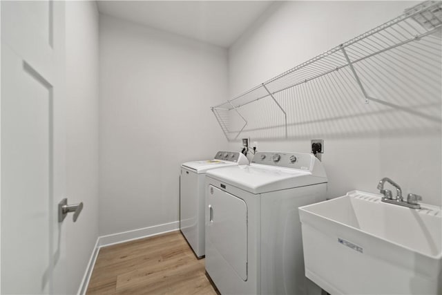 laundry room featuring sink, washing machine and clothes dryer, and light hardwood / wood-style floors