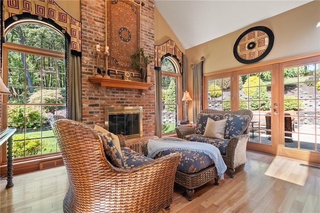 living area featuring hardwood / wood-style flooring, high vaulted ceiling, french doors, and a fireplace