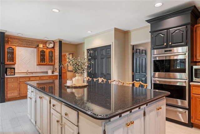 kitchen with sink, a center island, dark stone countertops, decorative backsplash, and stainless steel double oven