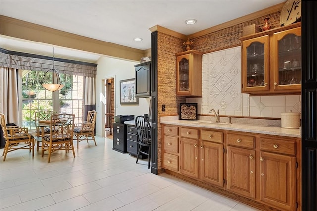 kitchen featuring tasteful backsplash, sink, ornamental molding, pendant lighting, and light stone counters