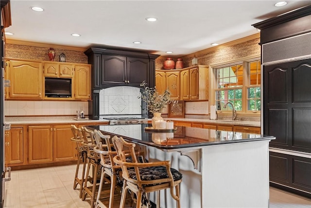 kitchen with a kitchen island, tasteful backsplash, sink, stainless steel gas cooktop, and a breakfast bar