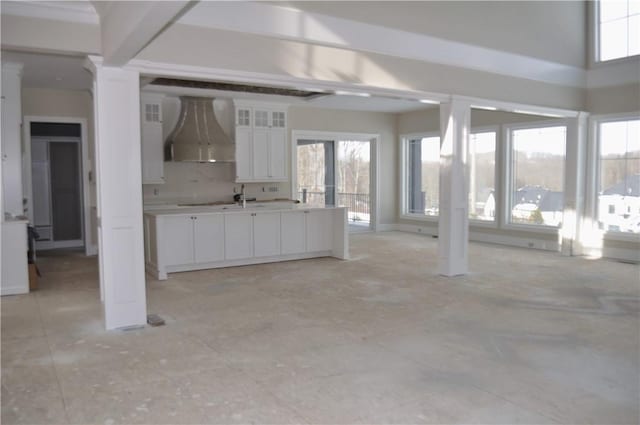 interior space featuring white cabinetry, wall chimney range hood, ornate columns, sink, and backsplash