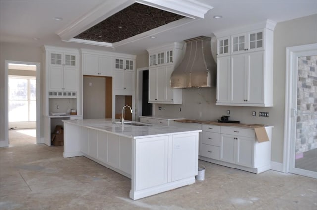 kitchen with sink, white cabinets, wall chimney exhaust hood, and an island with sink