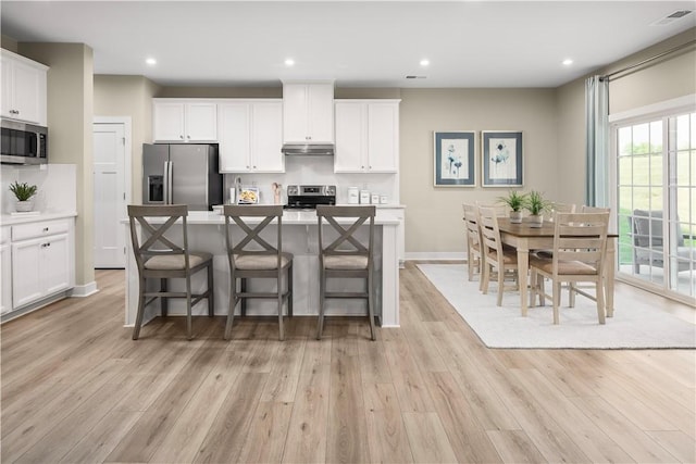 kitchen featuring appliances with stainless steel finishes, a kitchen island, white cabinetry, a breakfast bar, and light hardwood / wood-style flooring