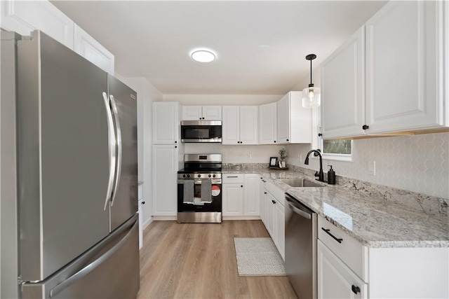 kitchen featuring appliances with stainless steel finishes, white cabinetry, sink, light hardwood / wood-style flooring, and pendant lighting