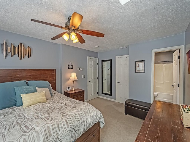 carpeted bedroom featuring ceiling fan, connected bathroom, and a textured ceiling