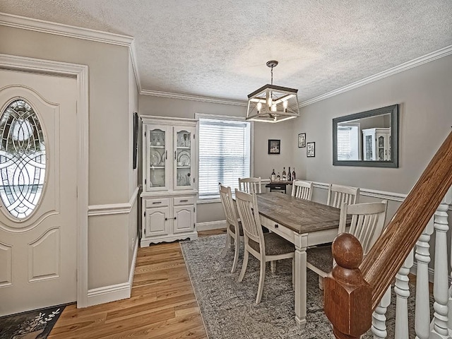 dining room featuring an inviting chandelier, ornamental molding, a textured ceiling, and light wood-type flooring