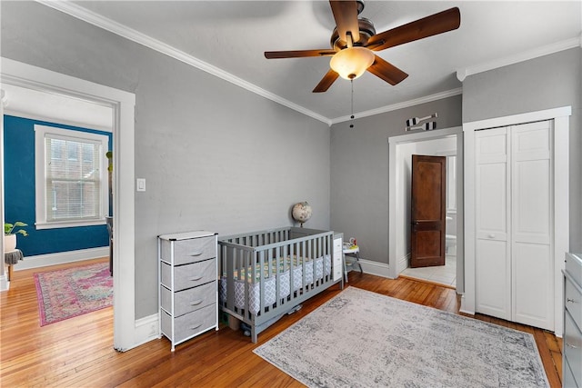 bedroom featuring a closet, a crib, ceiling fan, light hardwood / wood-style flooring, and crown molding