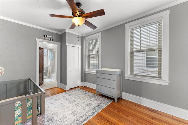 bedroom featuring crown molding, ceiling fan, a crib, light wood-type flooring, and a closet