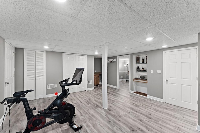 exercise room featuring light hardwood / wood-style floors and a drop ceiling