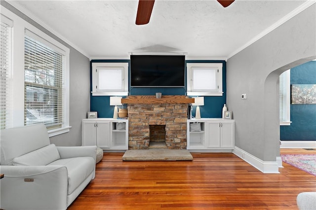 living room featuring a stone fireplace, hardwood / wood-style flooring, ceiling fan, and ornamental molding