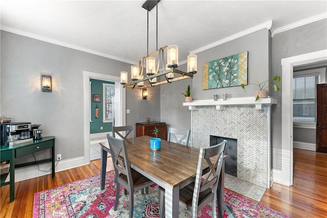 dining room featuring crown molding, a tile fireplace, hardwood / wood-style flooring, and a chandelier