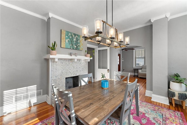 dining space with a tiled fireplace, hardwood / wood-style flooring, an inviting chandelier, and ornamental molding