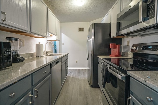 kitchen featuring light hardwood / wood-style floors, appliances with stainless steel finishes, a textured ceiling, sink, and gray cabinets