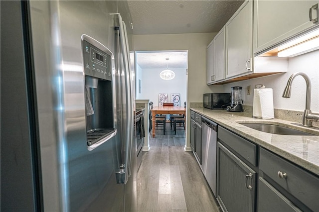 kitchen featuring a textured ceiling, appliances with stainless steel finishes, sink, gray cabinets, and light stone counters